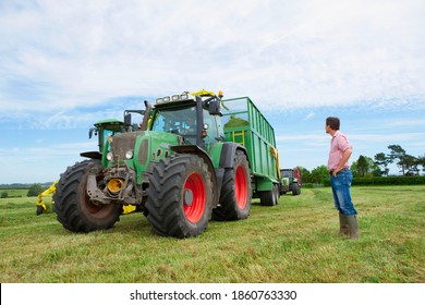 A Low Angle View Of A Farmer Looking Up At The Tractor And Trolley Collecting The Freshly Cut Hay In A Vast Farm Field