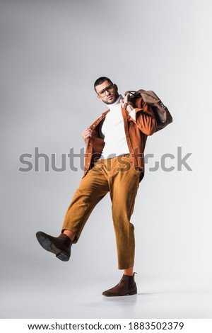 Low angle view of fashionable man holding brown bag and looking at camera on grey background 