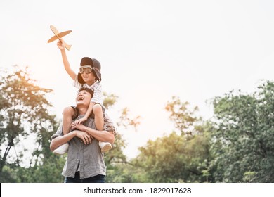 Low angle view of a father piggybacking his boy at sunset while he's playing with toy plane in park outdoors.happy adorable boy holding paper plane and sitting on his young active father shoulders. - Powered by Shutterstock