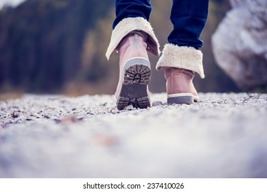 Low Angle View Of The Feet Of A Woman In Jeans And Ankle High Leather Boots Walking Along A Rural Path Away From The Camera, Vintage Effect Toned Image.