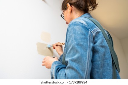 Low Angle View Of Female Architect Woman Testing Light Paint From Sample Pot On Renovated Room Wall During The General Reconstruction Of Dream House.