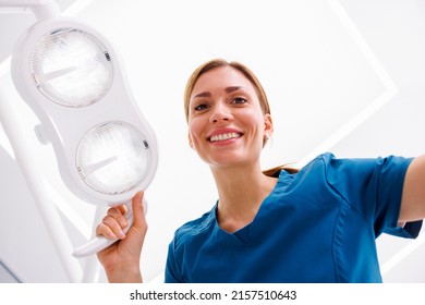 Low angle view of female dentist adjusting reflector lights above patient's head sitting in dental chair