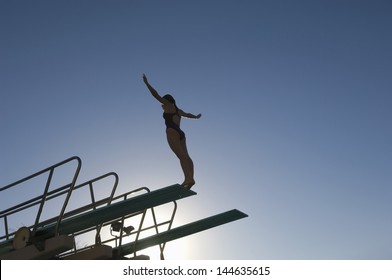Low angle view of a female diver with arms out about to dive against the blue sky