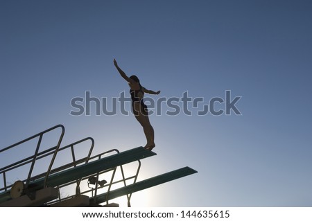 Low angle view of a female diver with arms out about to dive against the blue sky