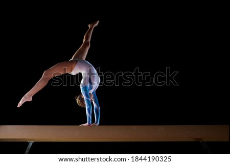 Low angle view of a female gymnast performing a handstand on a gymnastic balance beam.