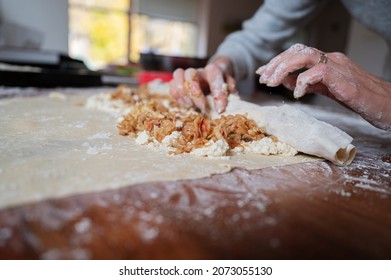 Low angle view of female hands rolling homemade apple strudel pastry on a dining table.