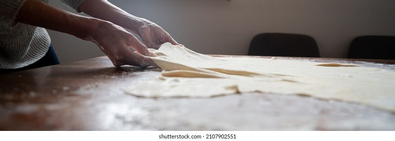 Low angle view of female hands pulling homemade vegan pastr dough for a traditional strudel on a dining table.