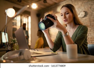 Low Angle View Of Female Photographer Looking At Photos On Camera While Working Late In The Office. 