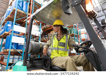 Low angle view of female staff driving forklift in warehouse. This is a freight transportation and distribution warehouse. Industrial and industrial workers concept