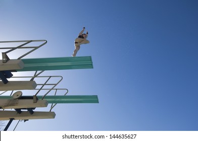 Low Angle View Of A Female Swimmer Preparing To Dive From Diving Board Against Clear Blue Sky