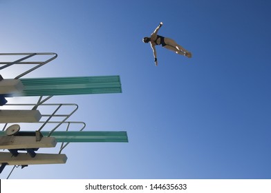 Low Angle View Of A Female Swimmer Preparing To Dive From Diving Board Against Clear Blue Sky