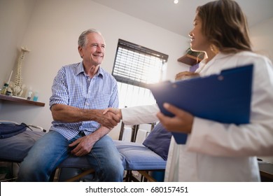 Low angle view of female therapist and senior male patient shaking hands at hospital ward - Powered by Shutterstock