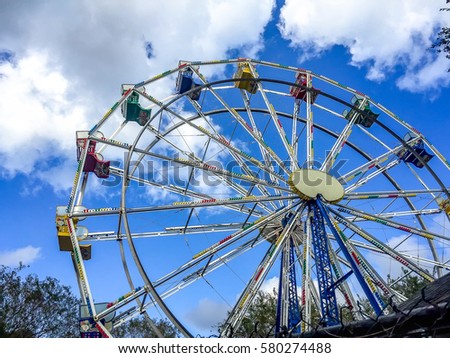 Low angle view of a ferris wheel in an amusement park with a blue sky background.  City park ferris wheel in Carousel Gardens Amusement Park, New Orleans City Park.