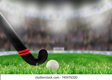 Low angle view of field hockey stick and ball on grass and deliberate shallow depth of field on brightly lit stadium background with copy space.