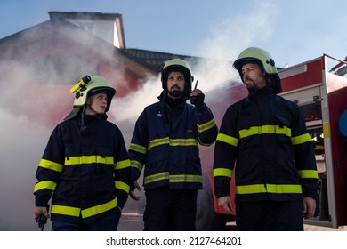 Low Angle View Of Firefighters Crew On Action With Fire Station And Truck In Background