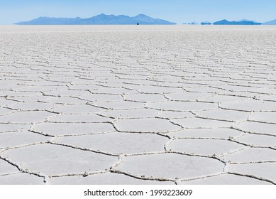 Low Angle View Of The Flat And Endless Landscape Of Uyuni Salt Desert In Bolivia, With A Car In The Distance And The Mountains With A Mirage Effect From The Heat.