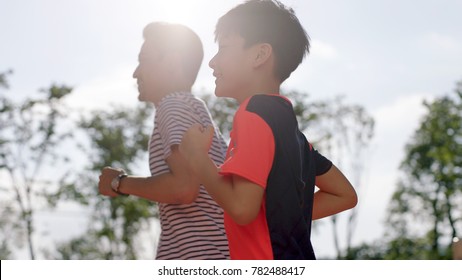 low angle view fo Chinese man & son jogging outdoors in garden back lighted - Powered by Shutterstock