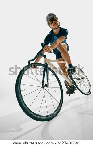 Low angle view of focused man, professional cyclist in motion, training, riding bicycle isolated on white background. Concept of sport, competition, active lifestyle, endurance
