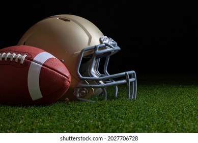 Low angle view of football and gold helmet on grass with dark background - Powered by Shutterstock