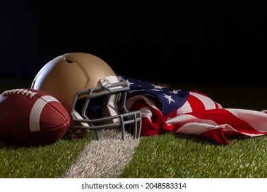 Low Angle View Of A Football, Helmet And American Flag On A Grass Field With Stripe And Dark Background