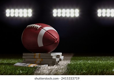 Low angle view of a football sitting on a pile of money on a grass field below stadium lights - Powered by Shutterstock