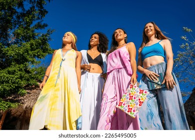 Low angle view of four models with colorful dresses standing on a tropical pool