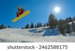 LOW ANGLE VIEW: Freestyle female snowboarder performing stylish indy grab trick. Young woman with snowboard jumping on kicker at snow park in mountain ski resort. Sunny winter day for snowboarding.