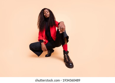 Low angle view full size photo of dark skin woman wear black boots red jacket isolated on beige color background - Shutterstock ID 1934360489
