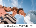 Low angle view of funny smiling teenagers standing and looking down at camera. Group of cheerful friends in casual clothes having fun together outdoors. Happy laughing boys and girls.