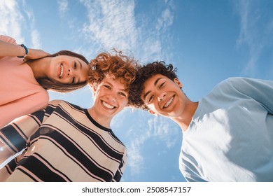 Low angle view of funny smiling teenagers standing and looking down at camera. Group of cheerful friends in casual clothes having fun together outdoors. Happy laughing boys and girls.