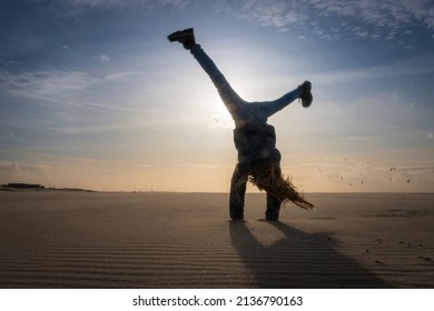 Low angle view of a girl having fun on a beach doing a cartwheel against the sun and blue sky with clouds
