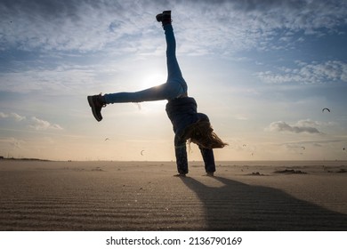 Low angle view of a girl having fun on a beach doing a cartwheel against the sun and blue sky with clouds