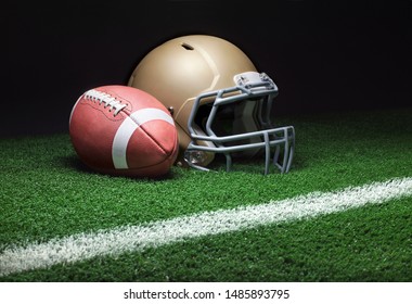 A low angle view of a gold football helmet with a football on a grass field with stripe and dark background - Powered by Shutterstock