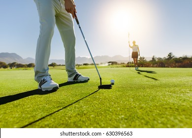 Low angle view of golfer on putting green about to take the shot. Male golf player putting on green with second female player in the background holding the flag. - Powered by Shutterstock