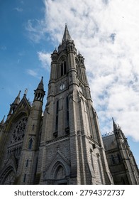 Low angle view of a Gothic cathedral tower with ornate stone architecture and dramatic clouds in a bright blue sky.