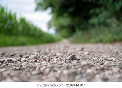 Low Angle View Of A Gravel Country Road Running Through Green Fields With A Focus To One Pebble.