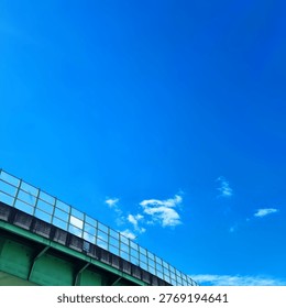 Low angle view of a green elevated highway sound barrier and lush trees against a bright blue sky with white clouds