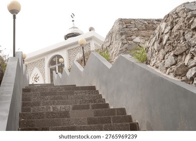 Low angle view of grey stone stairs leading up to a small white mosque with a silver dome situated on a rocky hill.