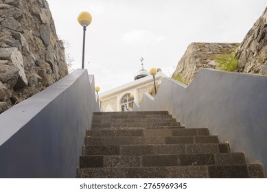 Low angle view of grey stone stairs leading up to a small white mosque with a silver dome situated on a rocky hill.