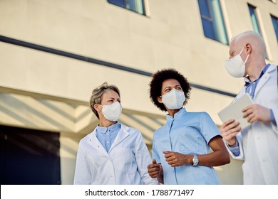 Low angle view of group of doctors talking outdoors while wearing face masks due to coronavirus epidemic.  - Powered by Shutterstock