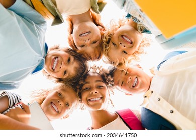 Low angle view of a group of mixed-race multi-ethnic classmates schoolchildren kids standing in round ring together smiling before classes lessons at school.