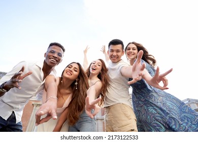 Low angle view of a group of multiracial friends looking at camera and smiling while having fun together outdoors. Friendship concept.