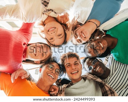 Low angle view of a group of multiracial friends standing on a circle, smiling and embracing together. Young teenagers laughing and looking at camera. Team of confident people on a coaching meeting