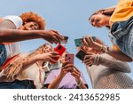 Low angle view of a group of smiling multiracial teenage women addicted to smartphones, watching videos, shopping online. Multiethnic young female people searching with apps on their mobile phones