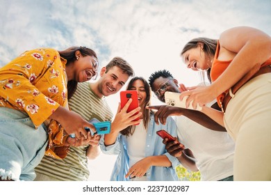 Low angle view of a group of smiling multiracial teenagers addicted to smartphones, watching funny videos, shopping online, enjoying outdoors. Multiethnic cheerful young people searching ,entertaining - Powered by Shutterstock