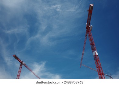Low angle view group of three red, yellow and blue tower cranes work over building construction site against clear blue sky.	