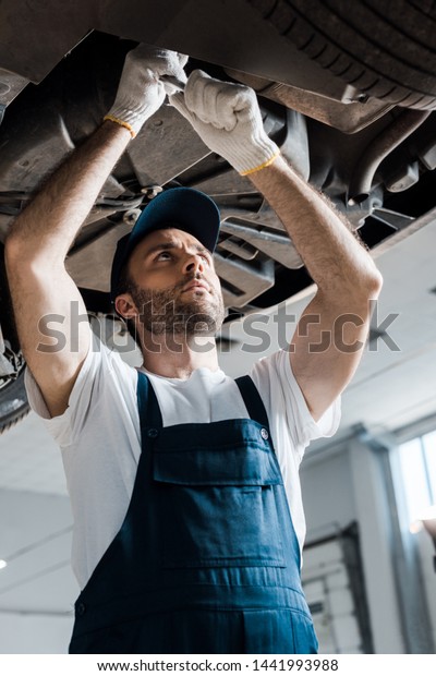 low angle view of handsome car mechanic\
repairing automobile in car service\
