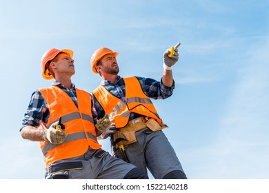 Low Angle View Of Handsome Constructor Pointing With Finger While Standing Against Blue Sky 