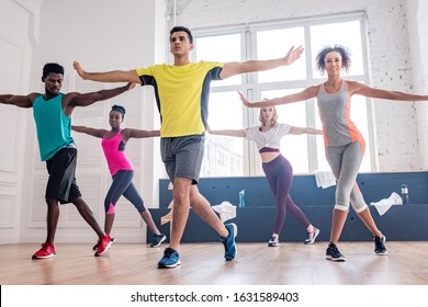 Low Angle View Of Handsome Trainer Performing Zumba With Multicultural Dancers In Studio