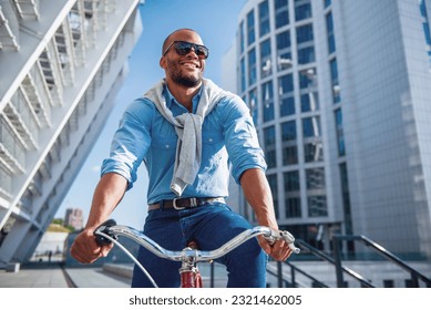 Low angle view of handsome young businessman in casual clothes and sun glasses riding his bike and smiling - Shutterstock ID 2321462005